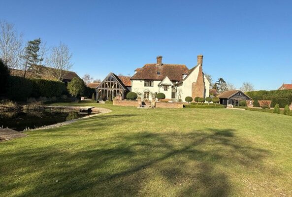 Listed manor house with a green lawn to the front and blue sky above