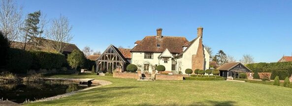 Listed manor house with a green lawn to the front and blue sky above
