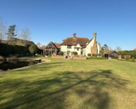 Listed Manor House with a green lawn to the front and blue sky above