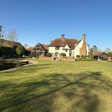 Listed Manor House with a green lawn to the front and blue sky above
